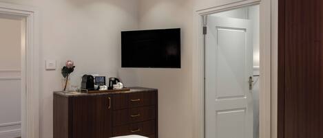 A hotel room with a bed, a dark wooden dresser, a flat-screen TV mounted on the wall, and a white door.