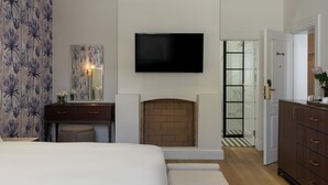 A bedroom with a bed, a dresser, a desk, a mirror, a fireplace, and a TV on the wall. - Guest House by Morea (Cape Town)