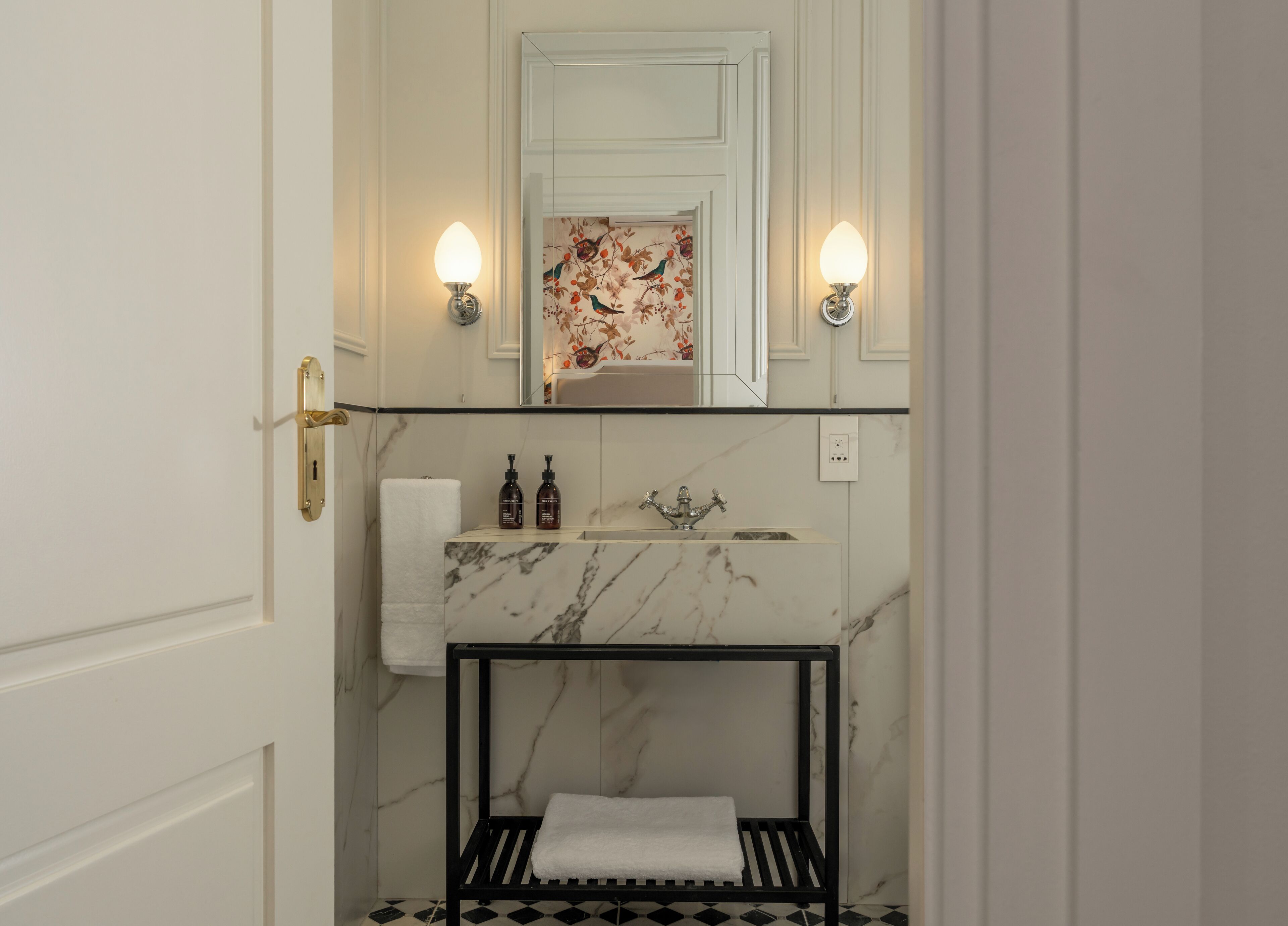A bathroom with a marble sink, two bottles of shampoo, a towel, and a black metal shelf.