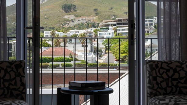 A room with a view of a mountain, a balcony with a table and chairs, and a patterned sofa. - Guest House by Morea (Cape Town)