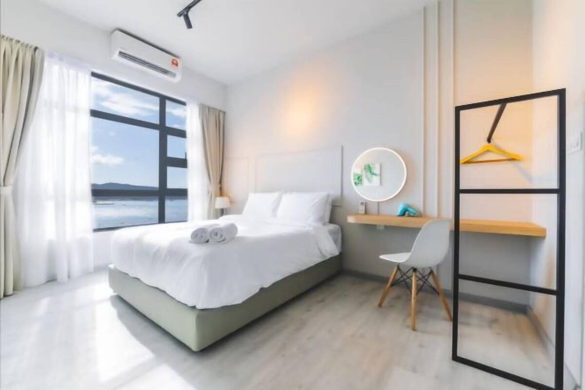 Moderni hotellihuone, jossa on suuri sänky, työpöytä, tuoli ja näkymä merelle.