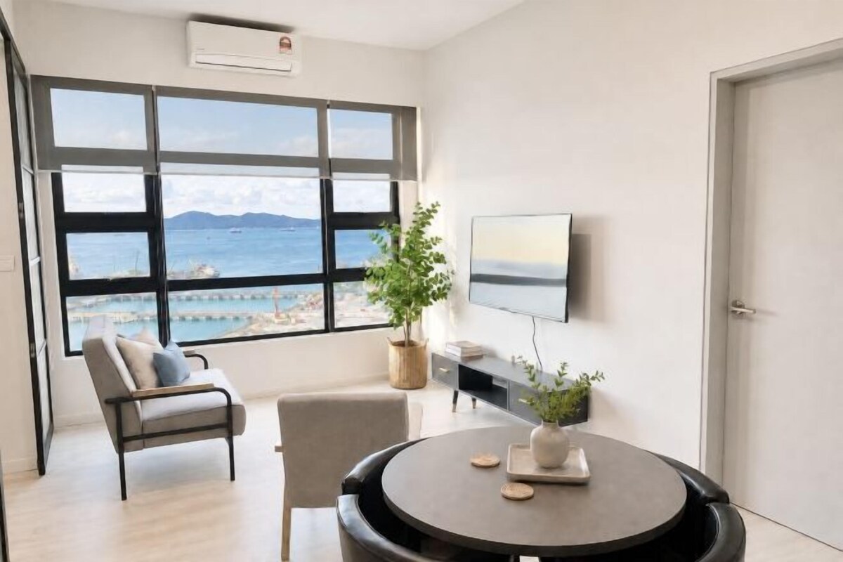 A modern room with a large window, a flat-screen TV, a round table, and a potted plant.