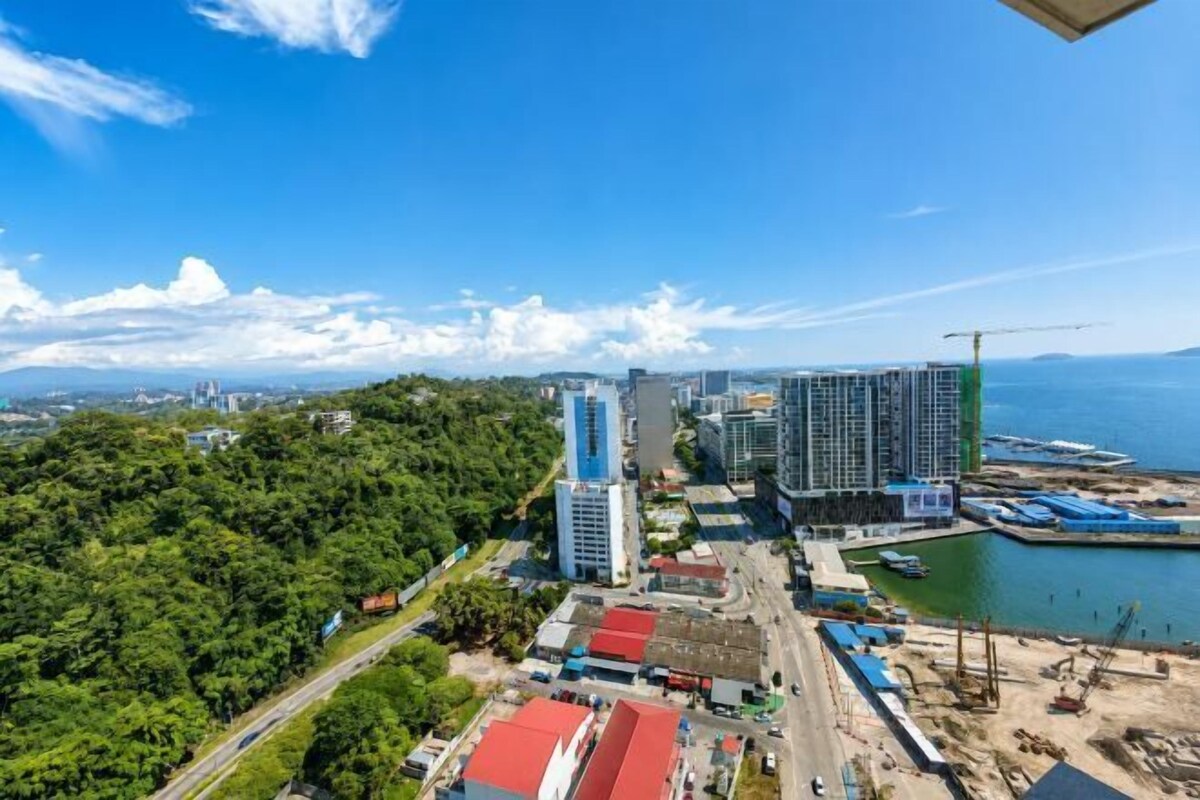 A coastal cityscape with high-rise buildings, a marina, and a forested area.