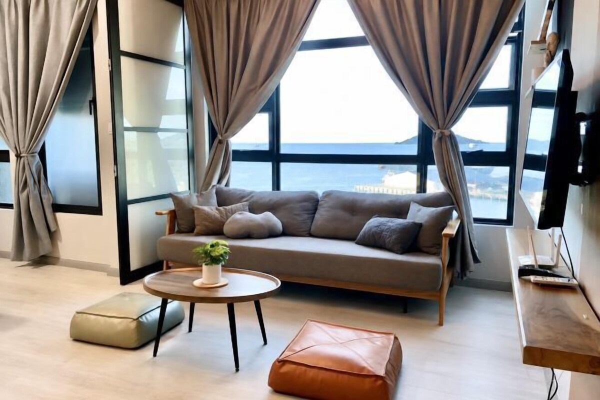 A modern living room with a sofa, a coffee table, and a view of the sea through large windows.