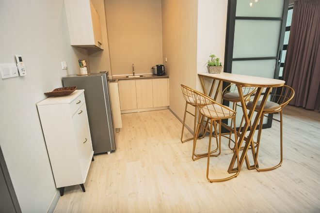 A compact kitchen with a refrigerator, sink, and wooden flooring. There is a small dining area with a table and chairs.