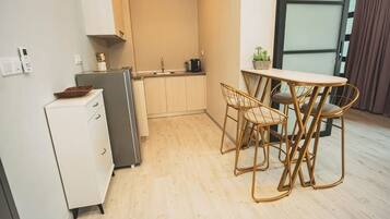 A compact kitchen with a refrigerator, sink, and wooden flooring. There is a small dining area with a table and chairs.