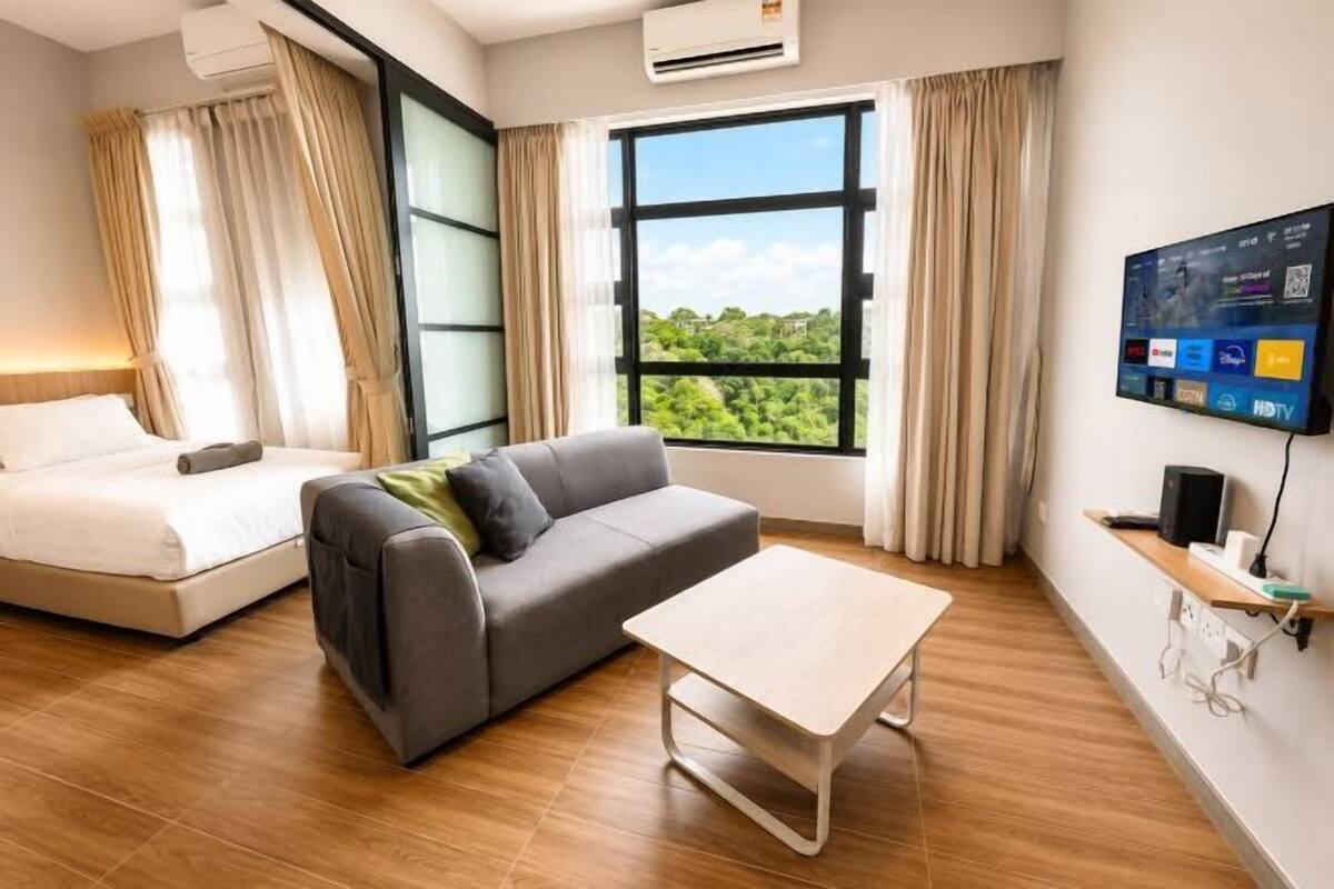 Hotellihuone, jossa on sänky, sohva, pöytä, televisio ja suuri ikkuna, josta on näkymä.