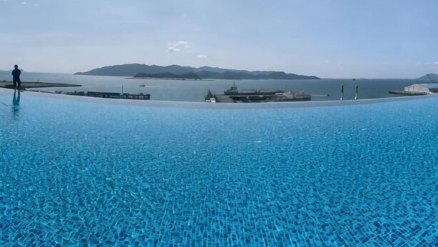 Une grande piscine extérieure à l’eau d’un bleu limpide, avec un quai et une vue lointaine sur la terre ferme, de l’autre côté de l’eau.