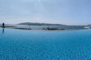 A large outdoor swimming pool with clear blue water, a dock, and a distant view of land across the water. - LS Sunset Ocean View Homestay - Jesselton Quay (Kota Kinabalu)