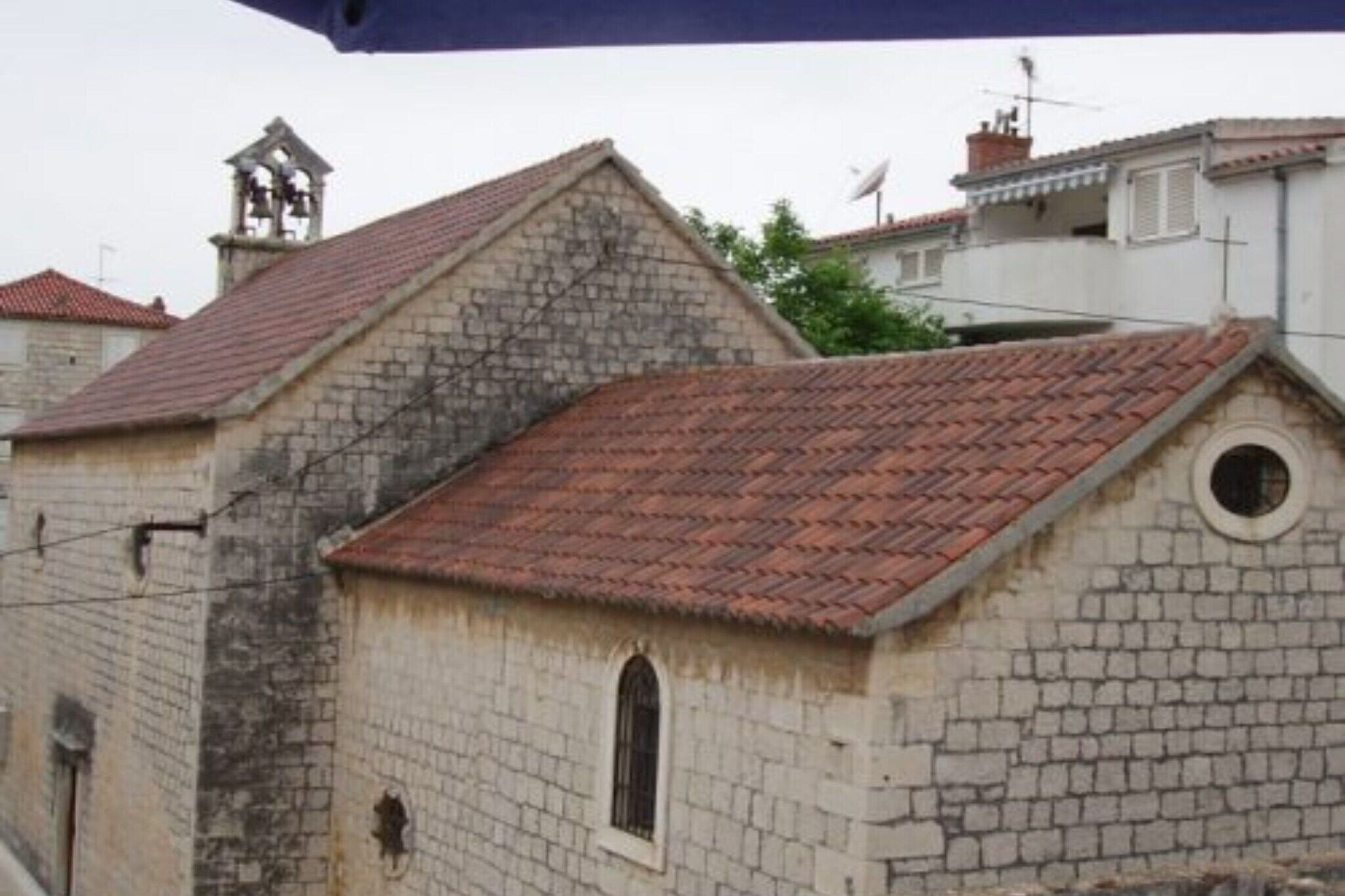 A stone building with a red-tiled roof, a bell tower, and a small window.