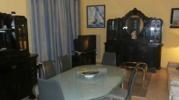 A dining area with a glass table, chairs, a television, and a decorative mirror.