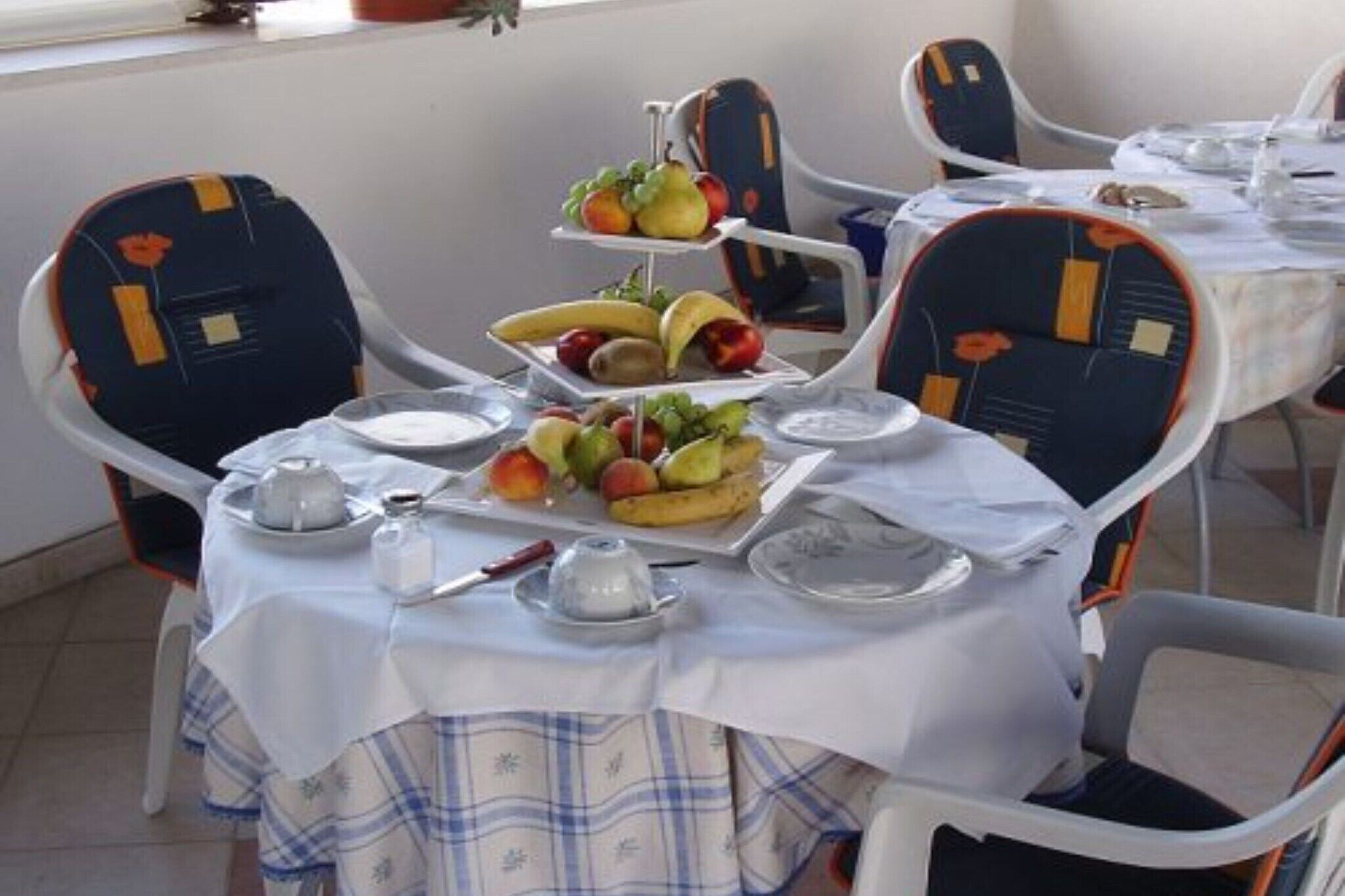 A dining area with a three-tiered fruit display, white tablecloths, and modern chairs with orange accents.