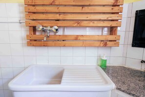 A bathroom with a white sink, a wooden shelf above the sink, and a green bottle on the countertop. - Tiny House in the Heart of the Madonie National Park   (Collesano)