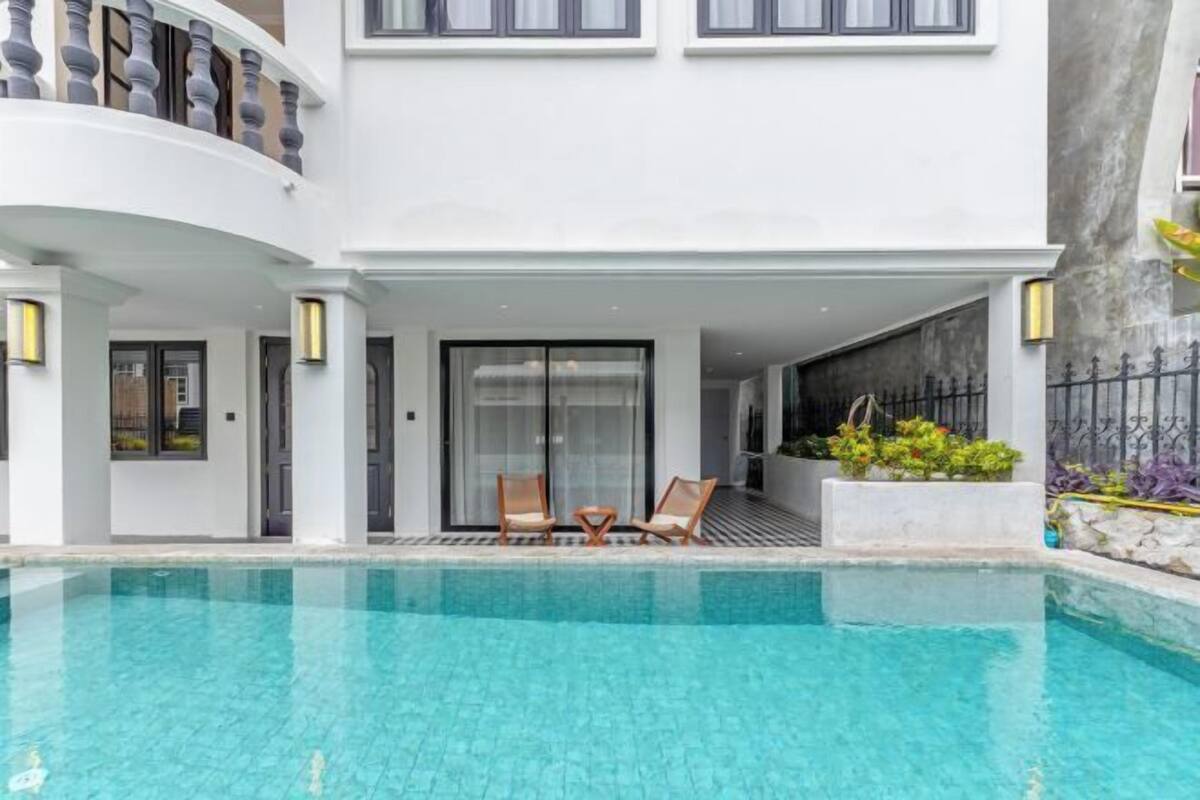 A modern building with a pool, two lounge chairs, and a balcony with a railing.