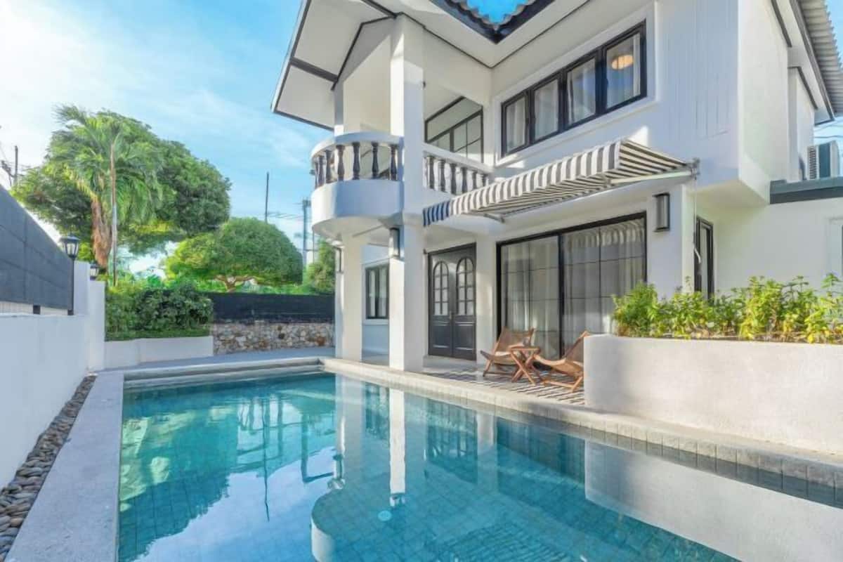 A modern two-story house with a swimming pool, a balcony, and a well-maintained garden.