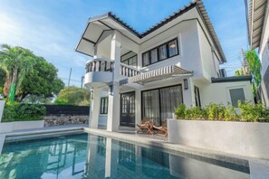 Ett modernt hus i två våningar med en swimmingpool, en balkong och en stenmur.