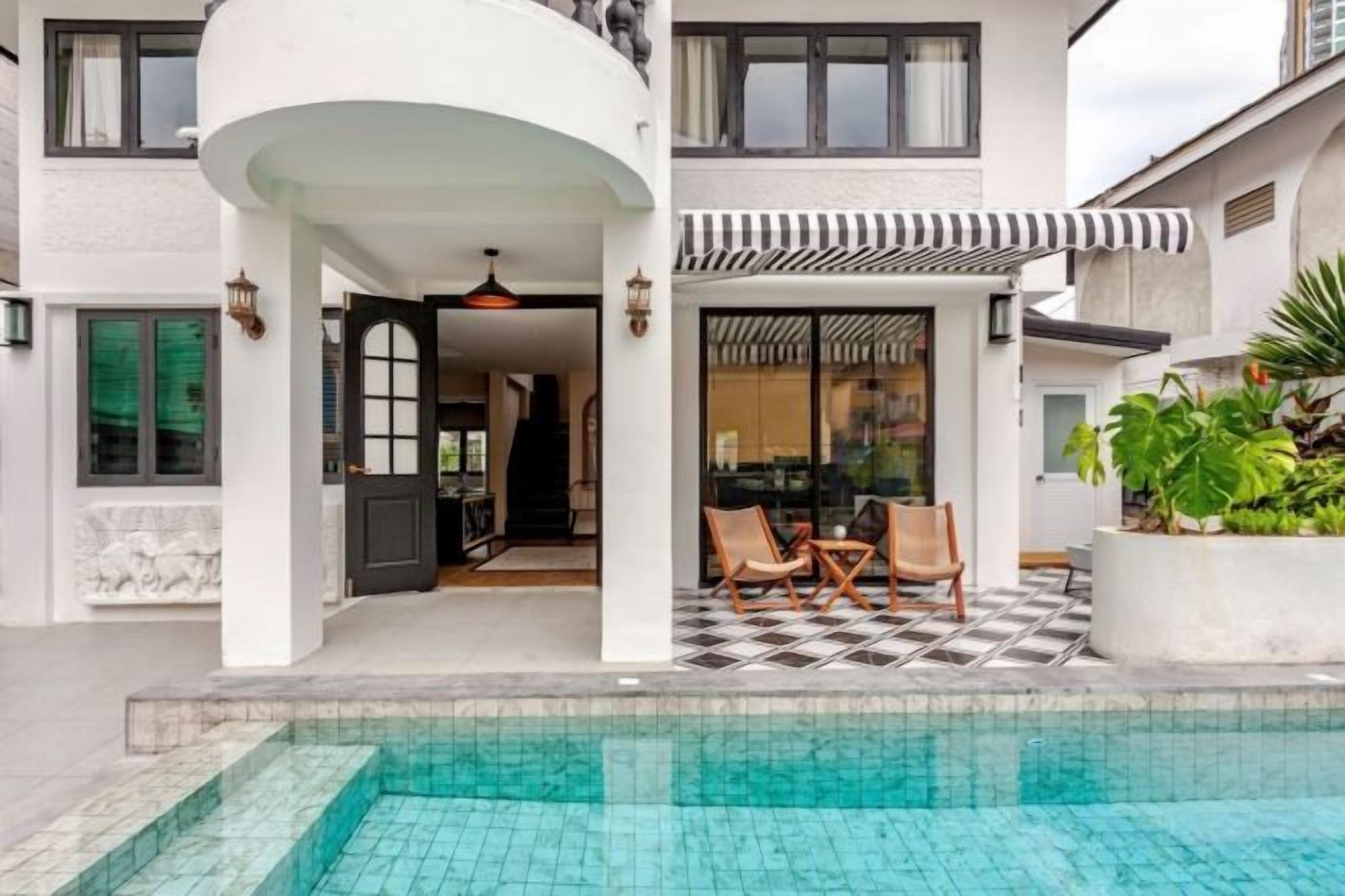 A two-story building with a swimming pool, outdoor seating, and a covered patio area.