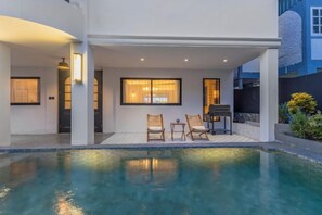 Ett modernt hus med en swimmingpool, utomhusmöbler och en väl upplyst uteplats.