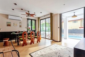 A spacious dining area with a large table and chairs, a ceiling fan, and a view of a swimming pool through glass doors. - Brunsvigia Pool Villa (Pattaya)