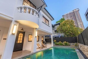 Ett modernt hus med en swimmingpool, en balkong och utsikt över en hög byggnad.