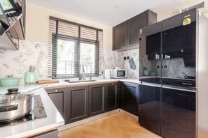A modern kitchen with dark cabinets, a stainless steel refrigerator, and a microwave. - Brunsvigia Pool Villa (Pattaya)