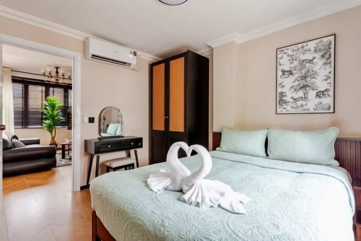 A hotel room with a bed, a desk, a chair, a mirror, a wardrobe, and a wall-mounted air conditioner.