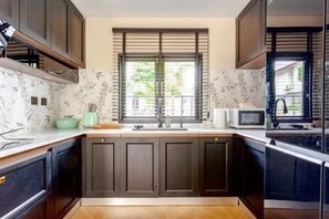 A kitchen with dark cabinets, a microwave, and a window with blinds. - Brunsvigia Pool Villa (Pattaya)