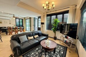 A modern living room with a black leather sofa, a coffee table, and a flat-screen TV. - Brunsvigia Pool Villa (Pattaya)