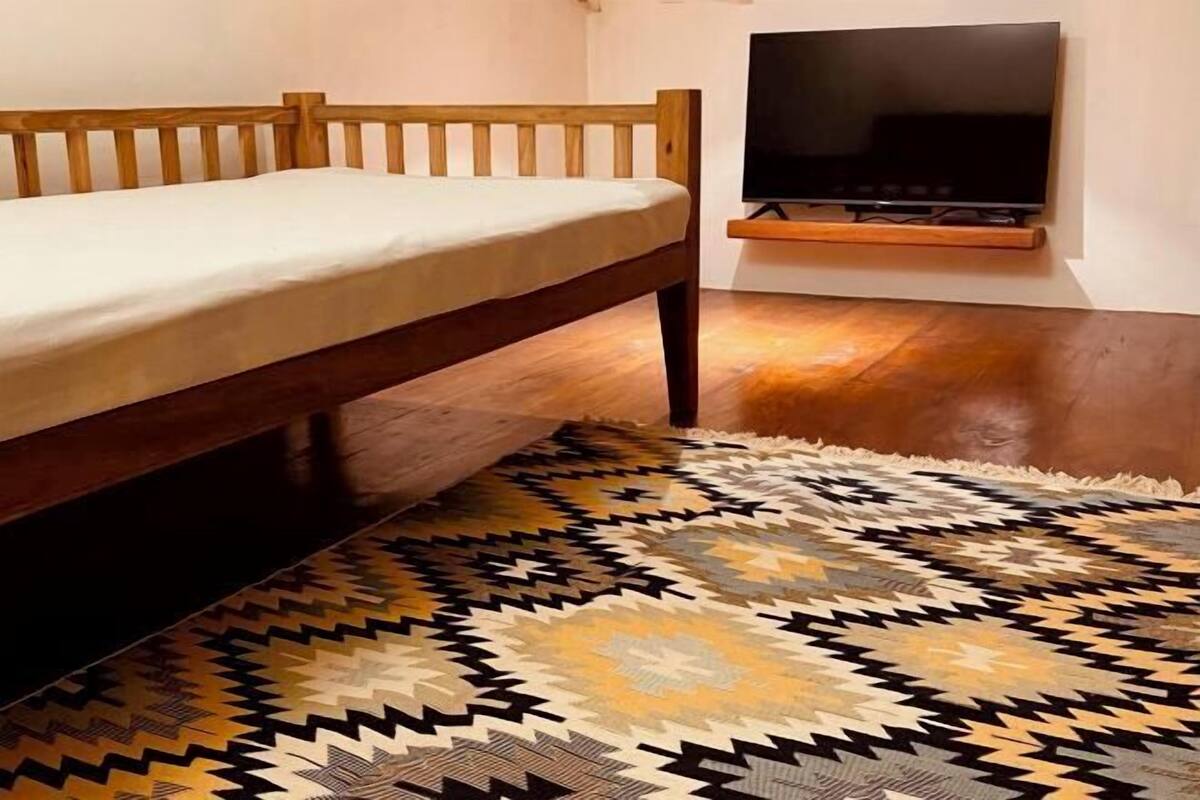 Een bed met een houten hoofdbord, een aan de muur bevestigde televisie en een kamerbreed tapijt met een patroon op de vloer.
