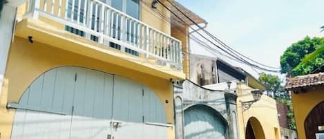 Un edificio giallo con un balcone bianco, un grande cancello bianco e un ingresso ad arco.