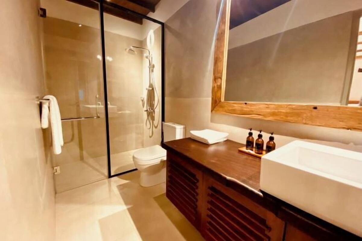 Een moderne badkamer met een douche met glazen wand, een houten wastafelmeubel met een ruime wastafel en een spiegel erboven.