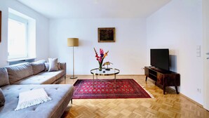 A living room with a sofa, TV stand, and a red patterned rug.
