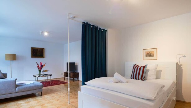 A modern hotel room with a large bed, a sofa, a small table with flowers, and a chair.