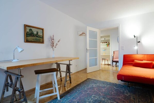 Une pièce comprenant un bureau en bois, une chaise, un canapé rouge, un tapis à motifs, un tableau et une armoire.