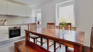 A modern kitchen with white cabinetry, a built-in oven, and a wooden dining table with chairs.