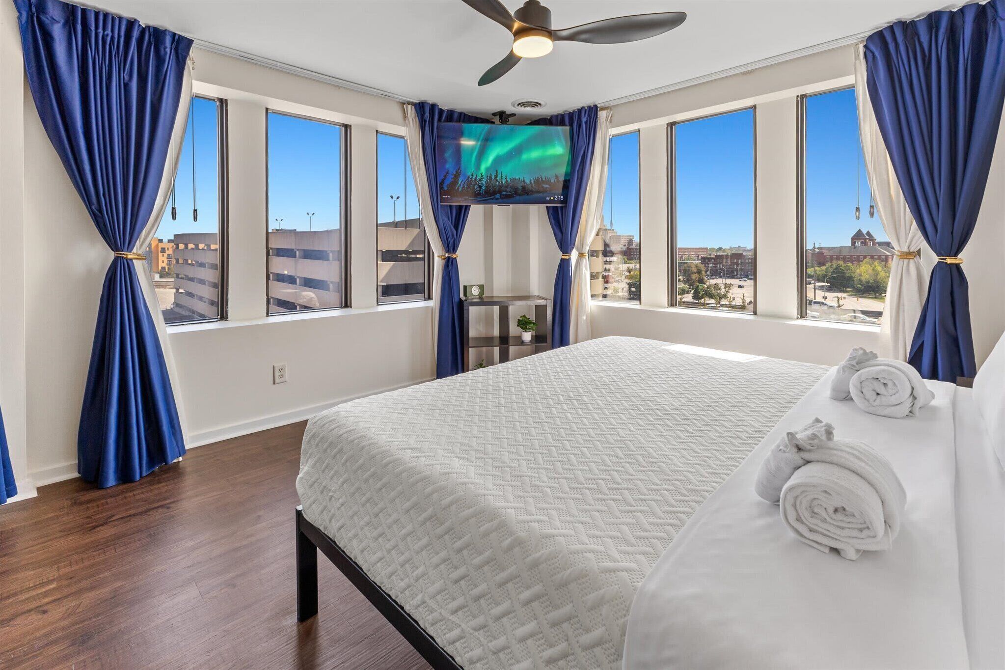 A hotel room with a bed, curtains, a ceiling fan, and a TV.