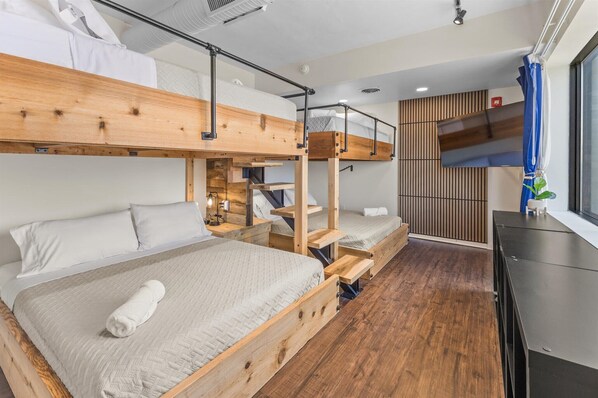 Une chambre avec un lit superposé, un plancher en bois, un bureau et une fenêtre avec des rideaux.