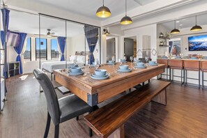 Un espace repas avec une table en bois dressée pour six personnes, des bancs et des luminaires suspendus.
