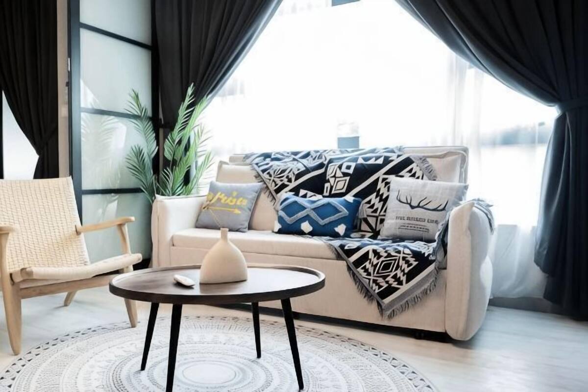 Una sala de estar moderna con un sofá, una mesita redonda, un sillón y un ventanal grande con cortinas.