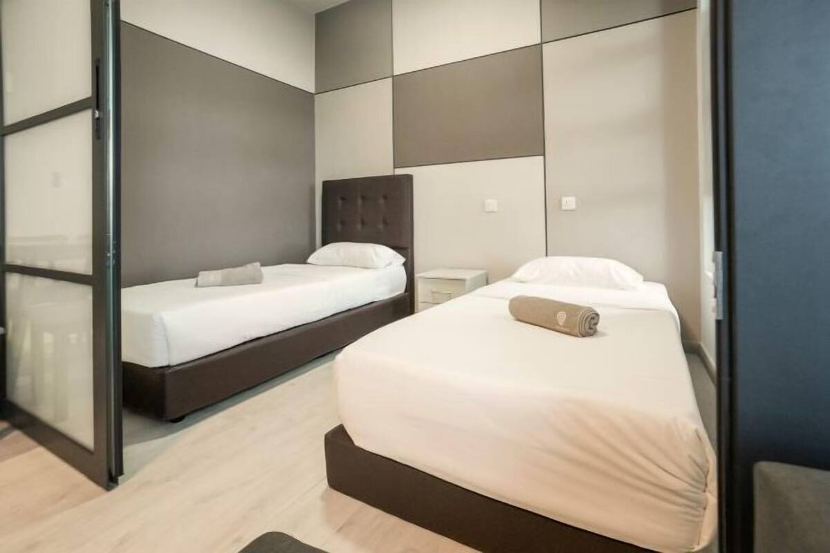 Una habitación de hotel moderna con una cama grande, una cama más pequeña, una mesita de noche y un ventanal corredero.