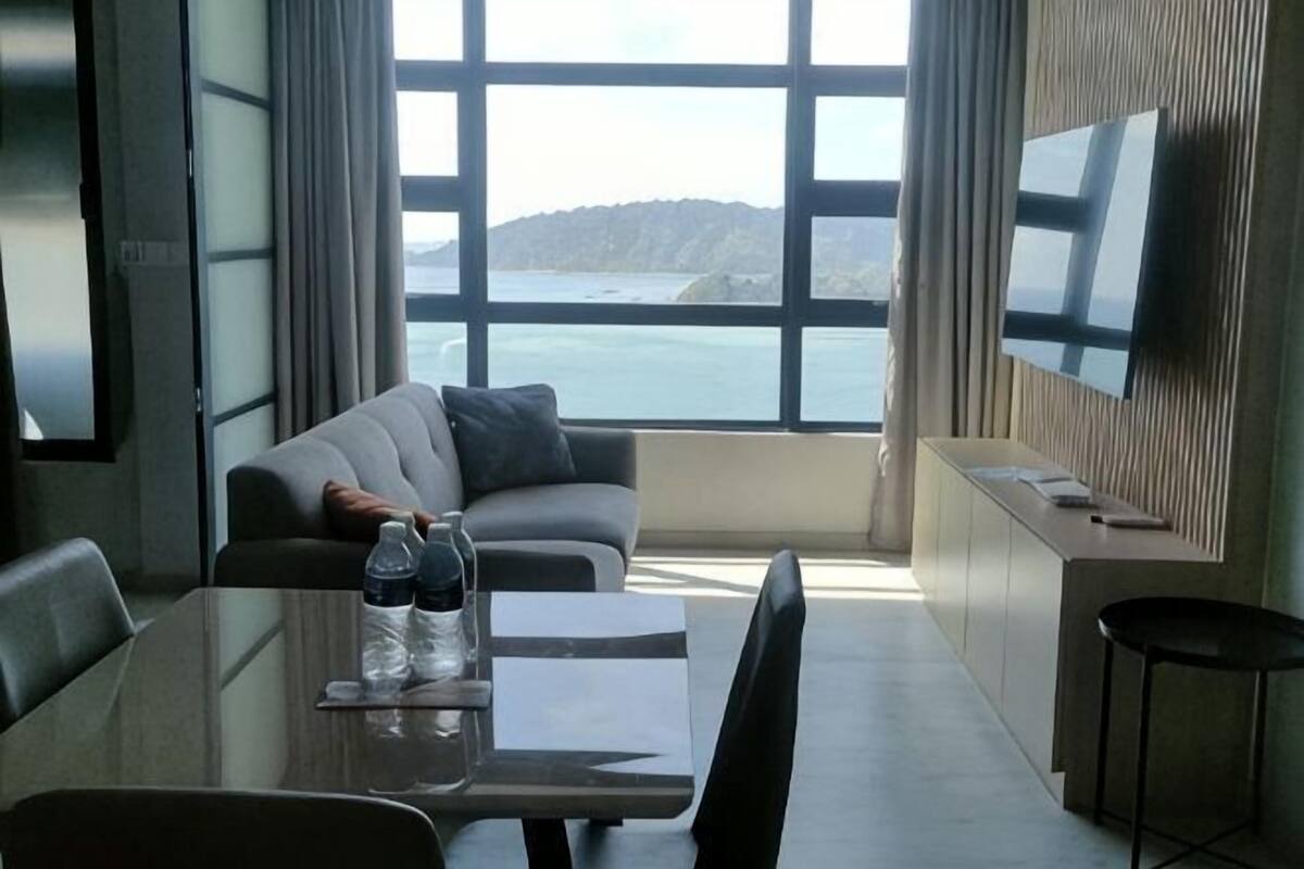 Una habitación de hotel moderna con un ventanal grande, un sofá, una mesa de comedor y un televisor montado en la pared.
