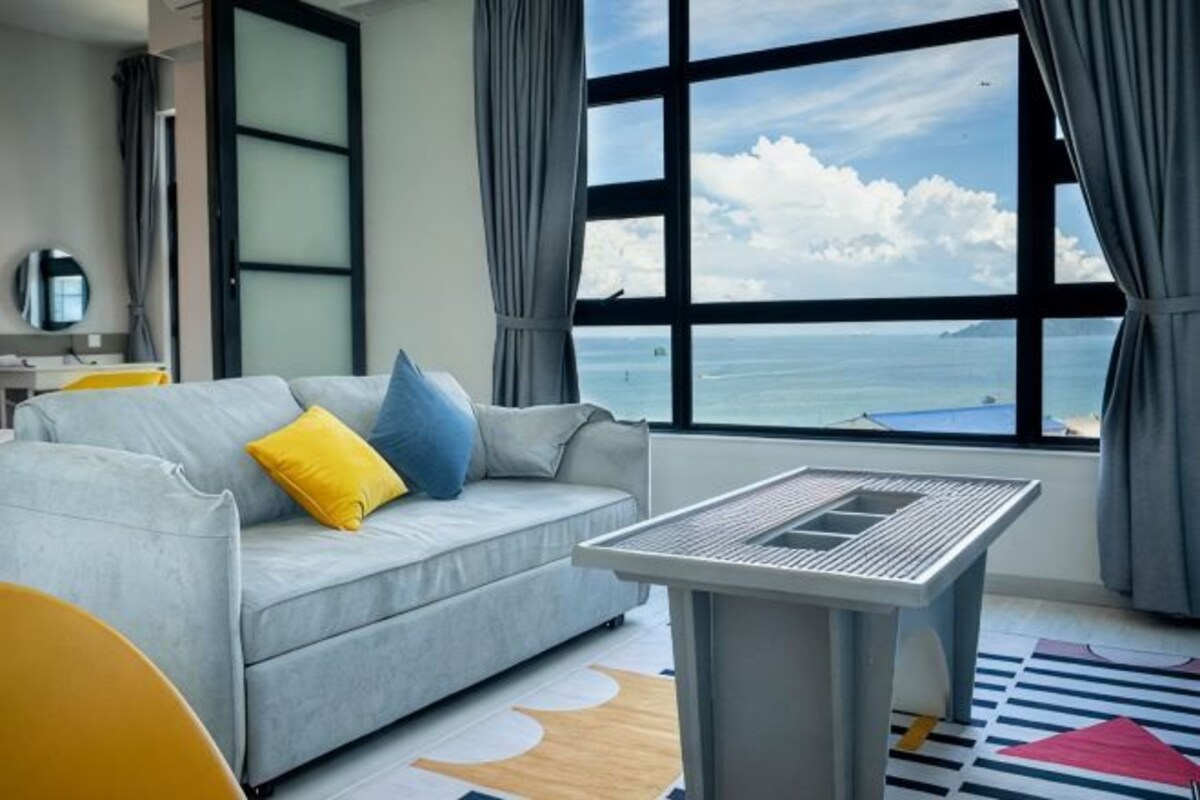 A modern living room with a sofa, a table, and a large window with a view of the sea.