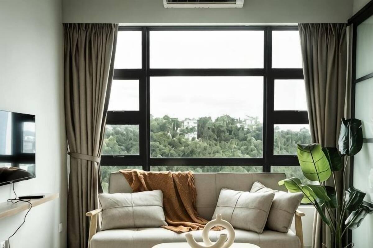Una habitación con un ventanal grande, un sofá, un televisor y una planta.