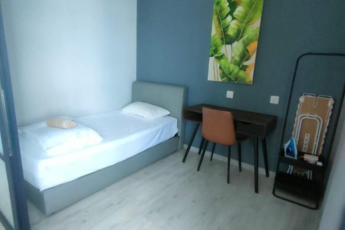 Una cama individual con colchón y almohada blancos, un escritorio con silla, un cuadro grande en la pared y un espejo.