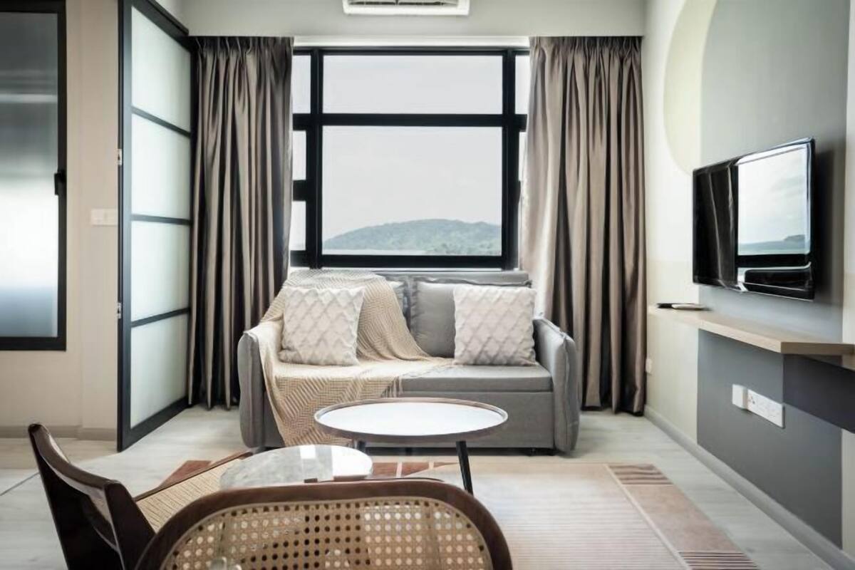 Una habitación moderna con sofá, televisión, una mesita y vistas amplias por una ventana grande.