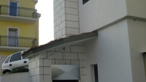 Um edifício de vários andares com fachada branca, uma varanda com guarda-corpo de metal e uma janela pequena.