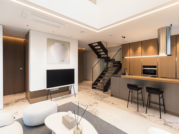 A modern kitchen with a built-in oven, a dining area with bar stools, a flat-screen TV, and a staircase leading to another level. - Caelum Black Gangnam Luxury Residence (Seoul)