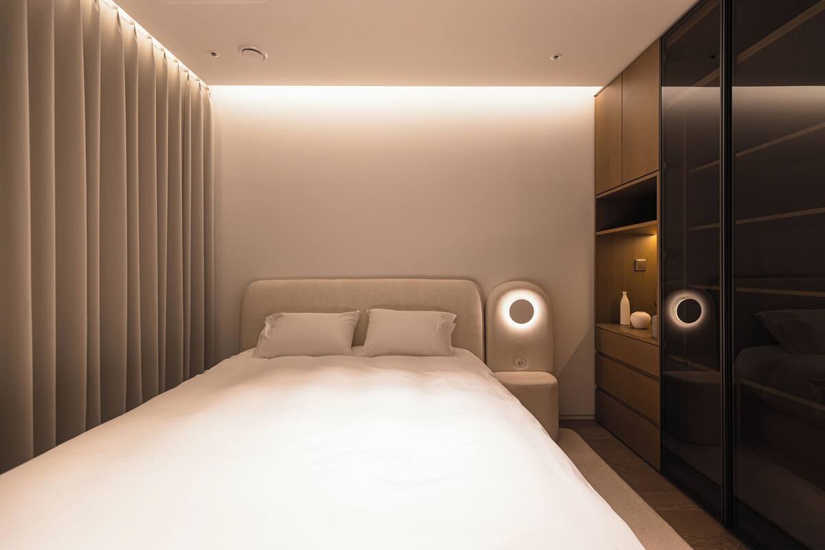 Ein modernes Schlafzimmer mit Bett, Nachttischen, einem Kleiderschrank und einer Wandleuchte.