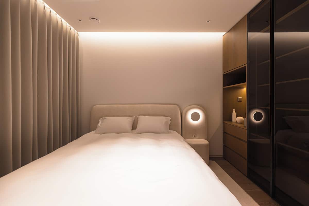 Um quarto moderno com uma cama, mesas de cabeceira, um guarda-roupa e um candeeiro fixado na parede.