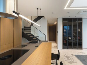 A modern kitchen with a wooden countertop, black chairs, a built-in stove, and a glass door leading to a living area with a sofa and bookshelves. - Caelum Black Gangnam Luxury Residence (Seoul)